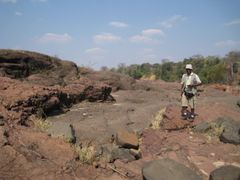 Professori Daúd Jamal seisoo pikriittilaavapaljastuman vieressä Luenha-joella Keski-Mosambikissa. Kuva: Jussi Heinonen.