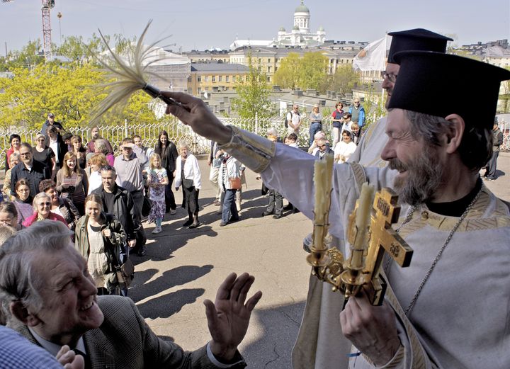 Pappi vihmoo pyhitetyllä vedellä ristisaatossa kulkevia seurakuntalaisia ja ohikulkijoitakin. Kuvassa pastori Mikko Leistola. Kuva: Valentin Kazerski.