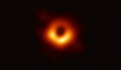 Kuvassa musta aukko näkyy vasten sen tapahtumahorisontin ympärillä pyörivää kuumaa kaasua, jonka säteilemää valoa voimakas painovoimakenttä taivuttaa. Kuva: EHT-yhteistyöhanke