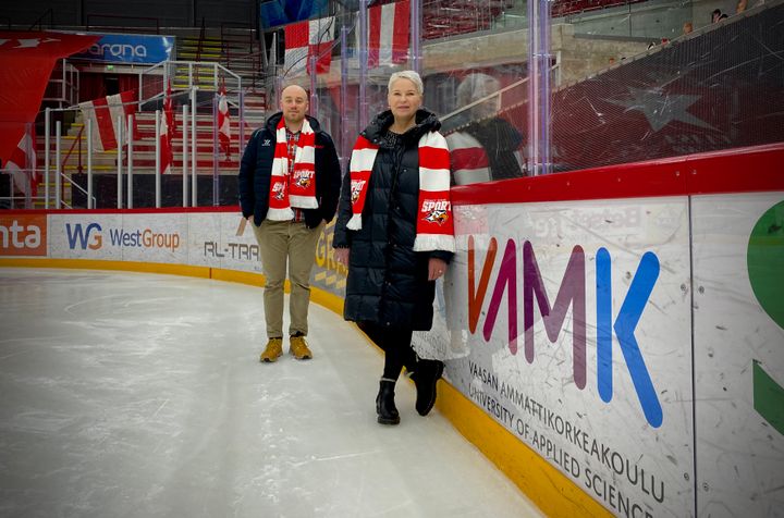 Juho Autio ja Kati Komulainen esittelevät VAMKin mainosta, joka koristaa Sportin kaukalon laitaa.