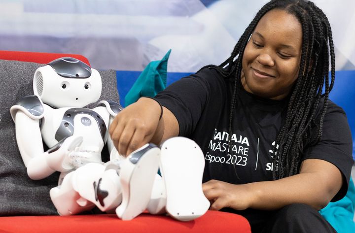 Catherine Nyamai som studerar för en dubbelexamen vid Omnia uppträdde som kund vid uppvisningsgrenen välfärdsteknologi och fick bekanta sig med en robot som kan vara en del av framtiden inom social- och hälsovårdsbranschen. Bild: Skills Finland / Kaisa Karvonen (Omnia).