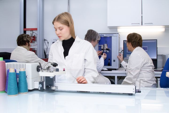 Arsenii Matarikin mittaa langan murtokuormitusta ja venymää. Unna Örn määrittelee langan kierrettä ja Terhi Nenonen mittaa kuidun vetolujuutta Marja Rissasen kanssa.