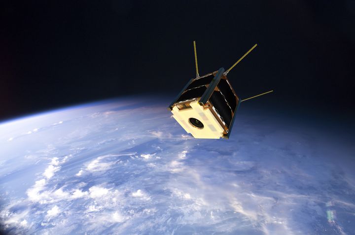 Hahmotelma Suomi 100 –satelliitista Maata kiertämässä. Kokeellinen 3D-tulostettu muoviosa on selvästi näkyvissä satelliitin etuosassa. Sen sisällä ovat radiotutkimuslaitteen antennit. Kamera linssi näkyy muoviosan keskellä. Kuva: Aalto-yliopisto