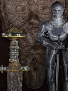 Kuvakollaasi: Merovingiaikainen miekka (650-750), saksalainen ratsumiehen haarniska (1530-1540), taustalla viikinkiaikainen Odin-koru. Kings&Guards Collection, kuvaaja Jouni Weckman