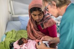Koshida Begum, 28, pitelee vastasyntynyttä lastaan, kun kätilö Jaana Laine mittaa vauvan hemoglobiinia. Kuva: Saara Mansikkamäki / Suomen Punainen Risti.