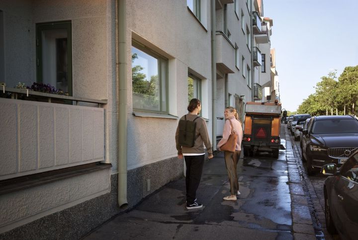Ihmiset keskustelevat kadulla ja takana näkyy lakaisukone