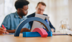 Kaksi ihmistä kokouspöydän ääressä, pöydällä etualalla sinisiä ja punaisia kaaria eli Tradekan logoelementtejä.