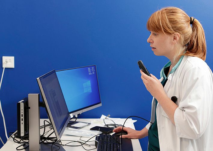 Lääkäri katsoo tietokoneen näyttöä ja puhuu mikrofoniin, joka tallentaa sanelun potilaskertomukseen.