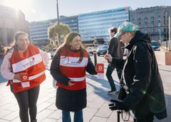 Två personer i Röda Korset-västar samlar in pengar från en förbipasserande på en gata.