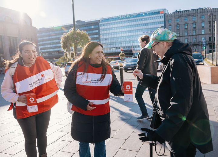 Två personer i Röda Korset-västar samlar in pengar från en förbipasserande på en gata.