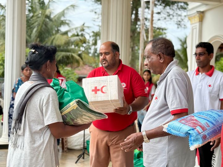 En person klädd i en röd tröja överlämnar en kartong till en person klädd i en grå T-shirt på en uteservering.