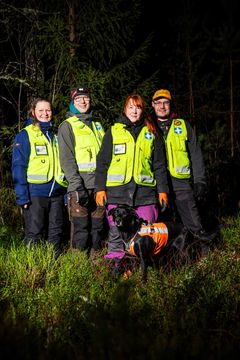 Fyra personer i räddningsvästar och en hund i skogsmiljö.