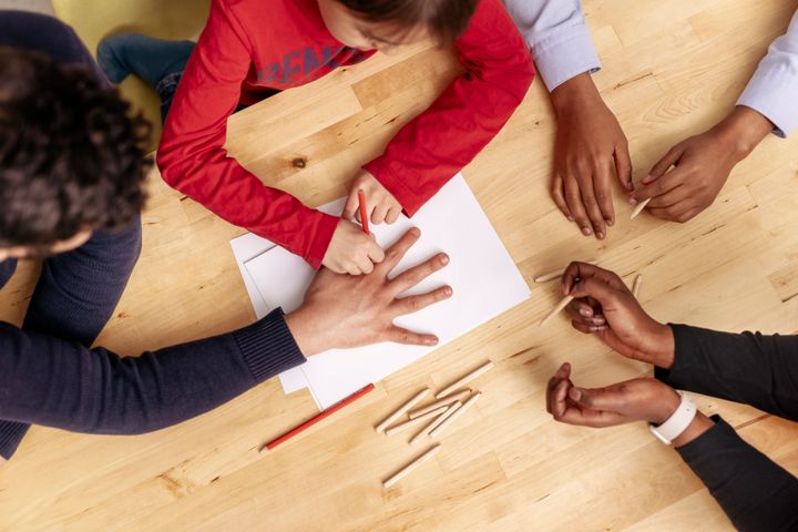 Kädet pöydällä, lapsi piirtää aikuisen käden ääriviivoja paperille