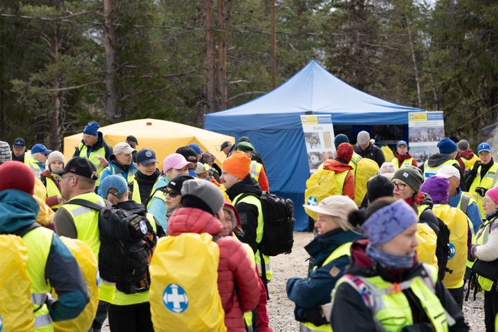 Joukko keltaliivisiä vapaaehtoisen pelastuspalvelun vapaaehtoisia kokoontuneina sinisen teltan ympärille.