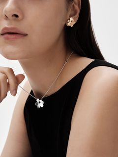 A woman wearing miniature jewelry from the Kalevala x Marimekko collaboration collection, including a necklace and earrings.