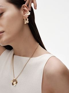 Naisella yllään Kalevala x Marimekko -yhteistyömalliston Unikko-teemaiset pronssikoru-uutuudet – kaula- ja korvakorut sekä ear cuff.