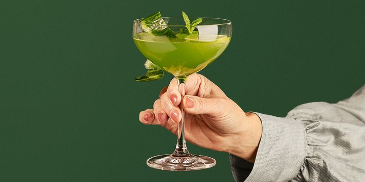 Henkilö pitää lasia, jossa on vihreä mocktail ja mintunlehtiä.