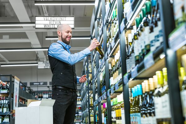 Myyjä hyllyttää viiniä Alkossa