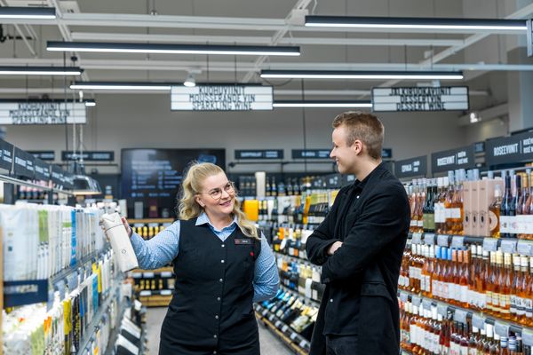 Iloinen Alkon myyjä esittelee tetraviiniä hyllystä asiakkaalle.