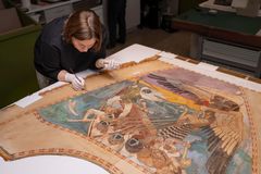 A paper conservator is applying paint to a large artwork with intricate designs, wearing gloves in a conservation workspace.
