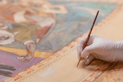 Alt text: A gloved hand applies water-soluble paint to repaired areas of a painting with a fine brush.