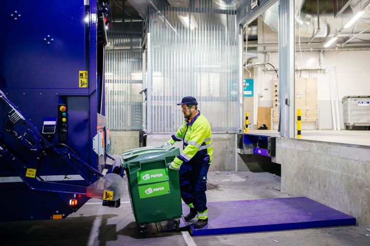 Mies kuljettaa pahvinkeräysastiaa jäteautoon
