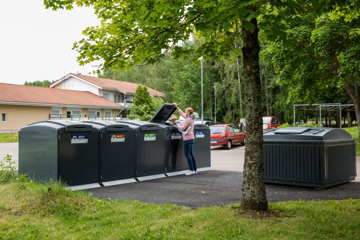 Nainen tiputtaa jätettä jäteastiaan kierrätyspisteessä, jossa on useita jäteastioita
