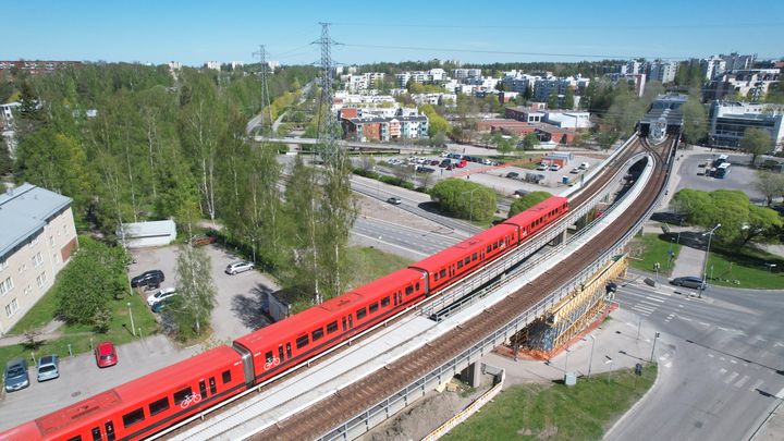 Ilmakuva metrojunasta Länsimäentien sillalla. Mellunmäen metroasema taustalla.