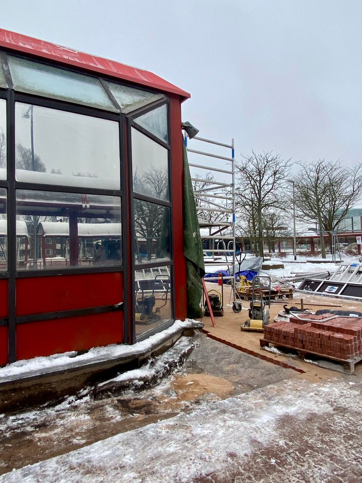 Punaisen rakennuksen vieressä oleva rakennustyömaa, jossa on lunta maassa. Taustalla on puita ja muita rakenteita.