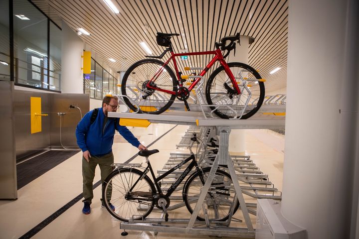Mies laittaa pyörää kaksikerroksiseen pyörätelineeseen sisätiloissa.