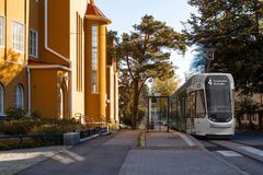 Havainnekuva raitiovaunusta pysäkillä, toisella puolella keltainen talo.