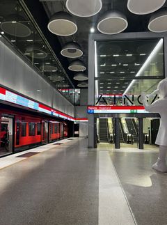 Metroasema, jossa on punainen metrovaunu. Taustalla liukuportaat ja opaste Tapio, Hagalund.