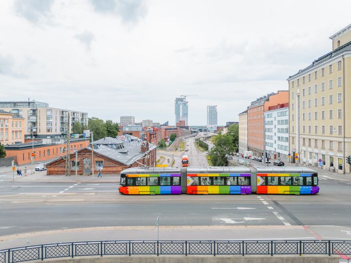 Raitiovaunu, joka on teipattu sateenkaaren väreillä, kulkee kaupungin kaduilla kesäpäivänä.