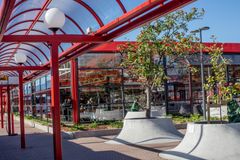 Punaisen katoksen suojassa oleva bussipysäkki, taustalla metroaseman suuret ikkunat ja istutettuja puita edustalla.