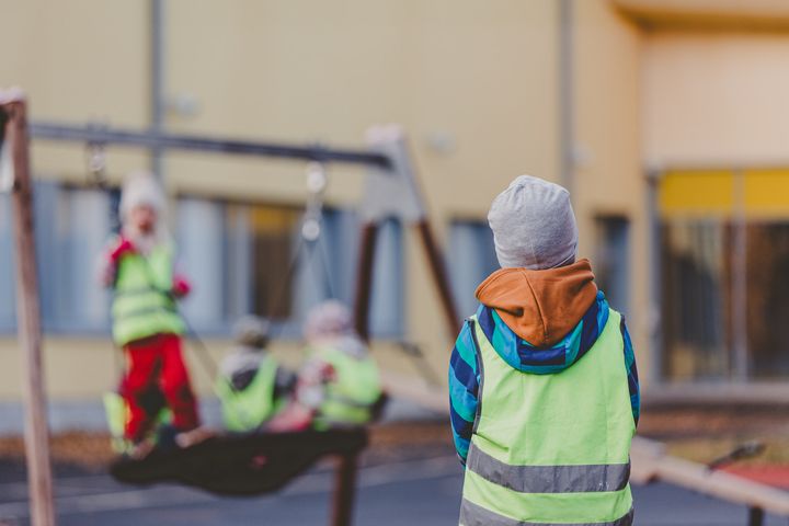 Kolme lasta leikkivät ulkona kirkkaanvärisissä huomioliiveissä.