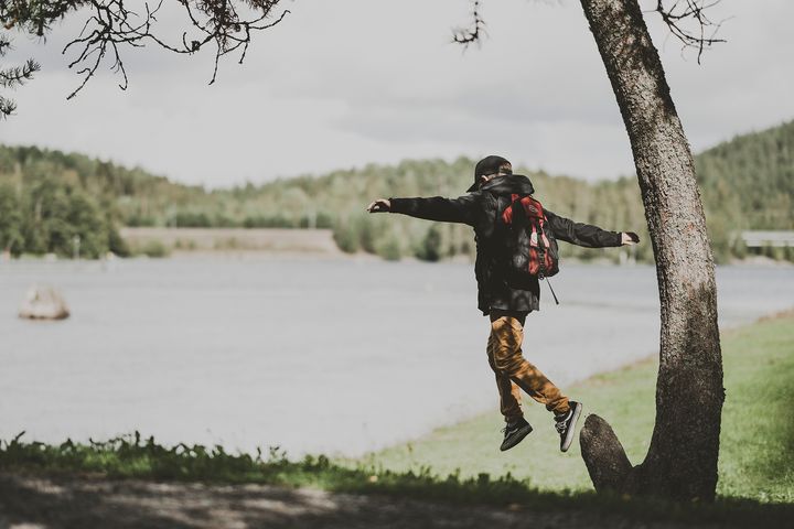 Poika hyppää kannolta, luonnon maisema taustalla.