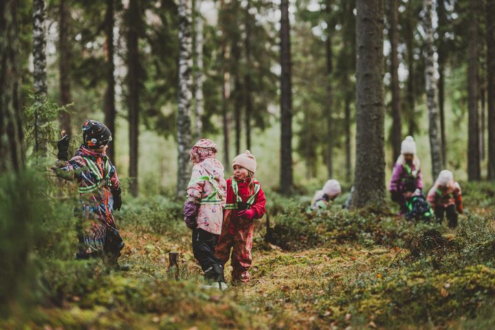 Barn leker i en skog, klädda i färgglada vinterkläder.