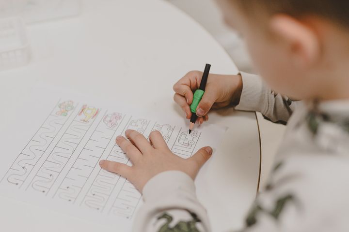 Lapsi tekee kynällä ja paperilla tehtävää pöydän ääressä.