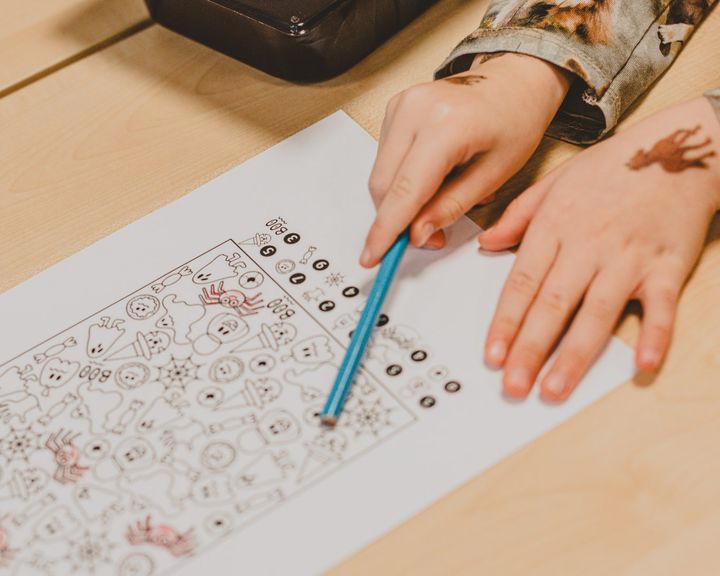 Lapsi pitää kynää ja tekee tehtävää monimutkaiselta vaikuttavalla väritystehtäväsivulla.