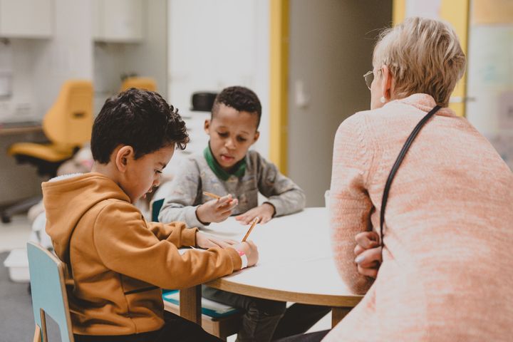 Kaksi lasta istuu pöydän ääressä aikuisen kanssa.