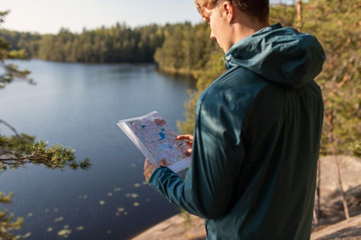 Nuori mies katsoo karttaa kalliolla Nuuksiossa suunnistaessa.