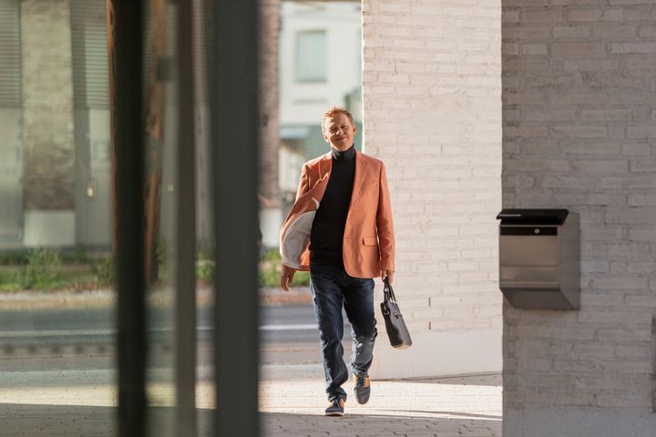 Mies kävelee ulkona kohti työpaikan sisäänkäyntiä salkku kädessä.
