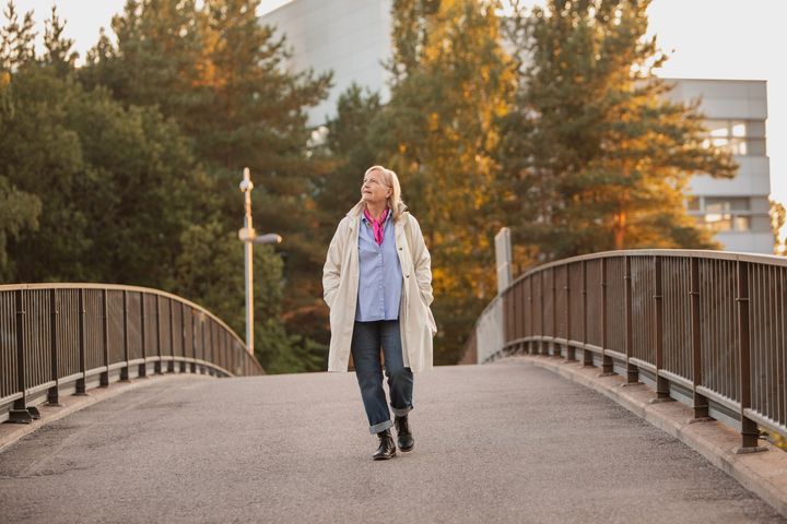 Valokuvassa nainen kävelee sillalla syksyisessä maisemassa.