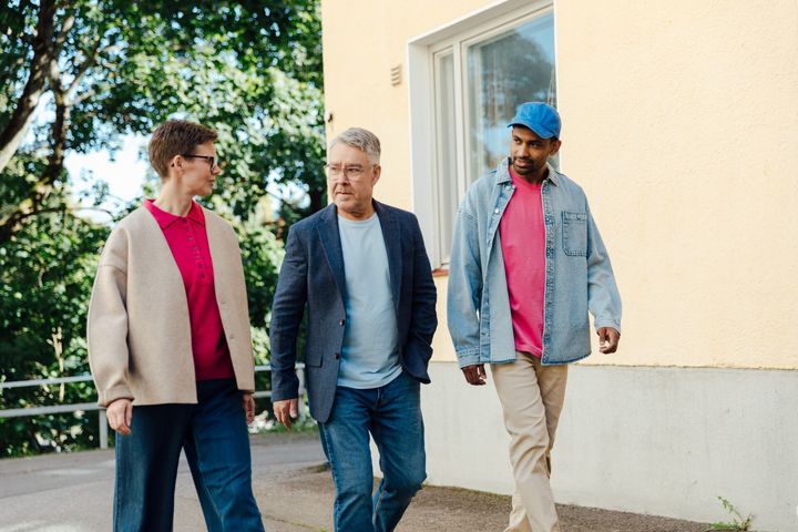 Valokuvassa kolme henkilöä kävelee kadulla ja keskustelee.