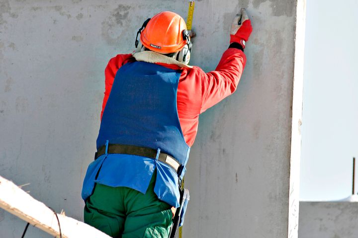 Valokuvassa rakennusmies mittaa betonielementtiä rakennustyömaalla.