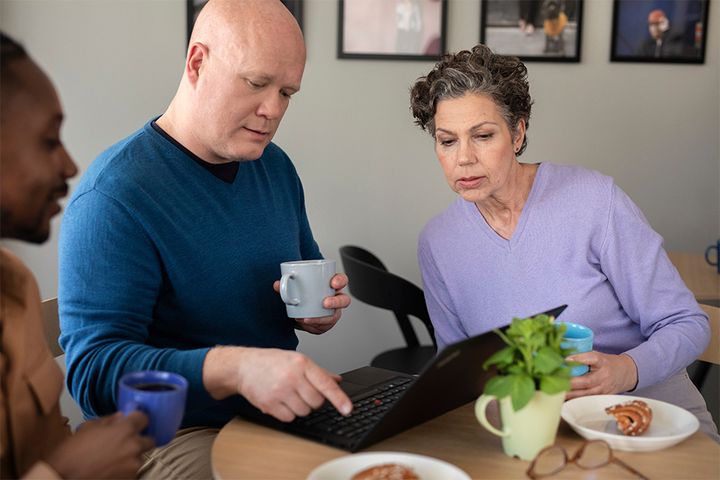 Työntekijät työpaikan kahviossa läppärin äärellä.