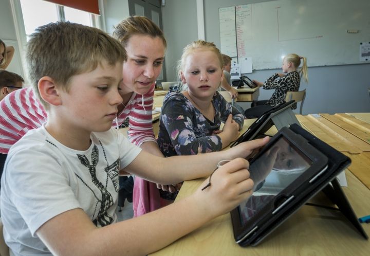 Valokuva, jossa lapsi käyttää tablettia luokkahuoneessa opettajan kanssa.