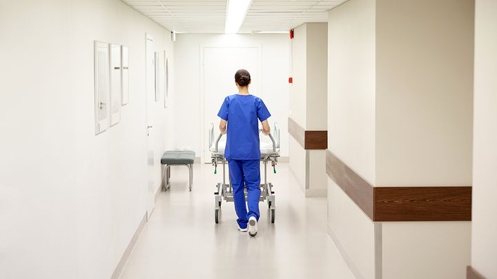 Työntekijä kuljettaa sairaalasänkyä käytävällä.