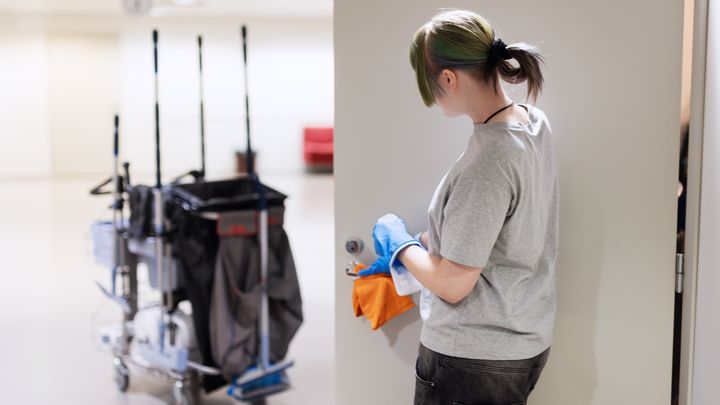 Henkilö puhdistaa ovenripaa, vieressä siivouskärry.