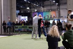 Kaksi ihmistä halaamassa golfmessuilla sisätiloissa, yleisöä taustalla.
